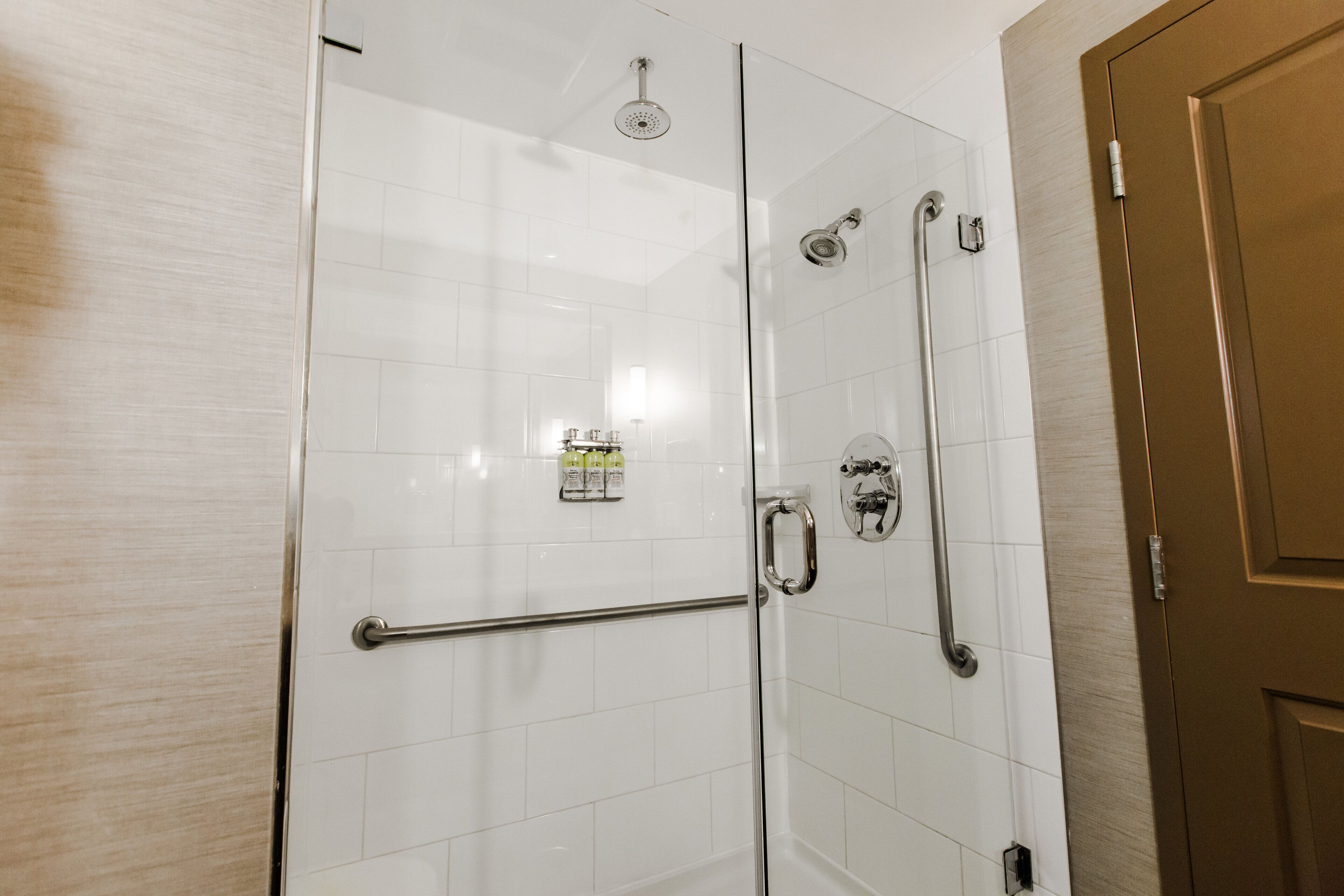 Une cabine de douche fermée par des parois en verre, équipée d’une barre d’appui, d’un pommeau de douche et d’un robinet fixé au mur.