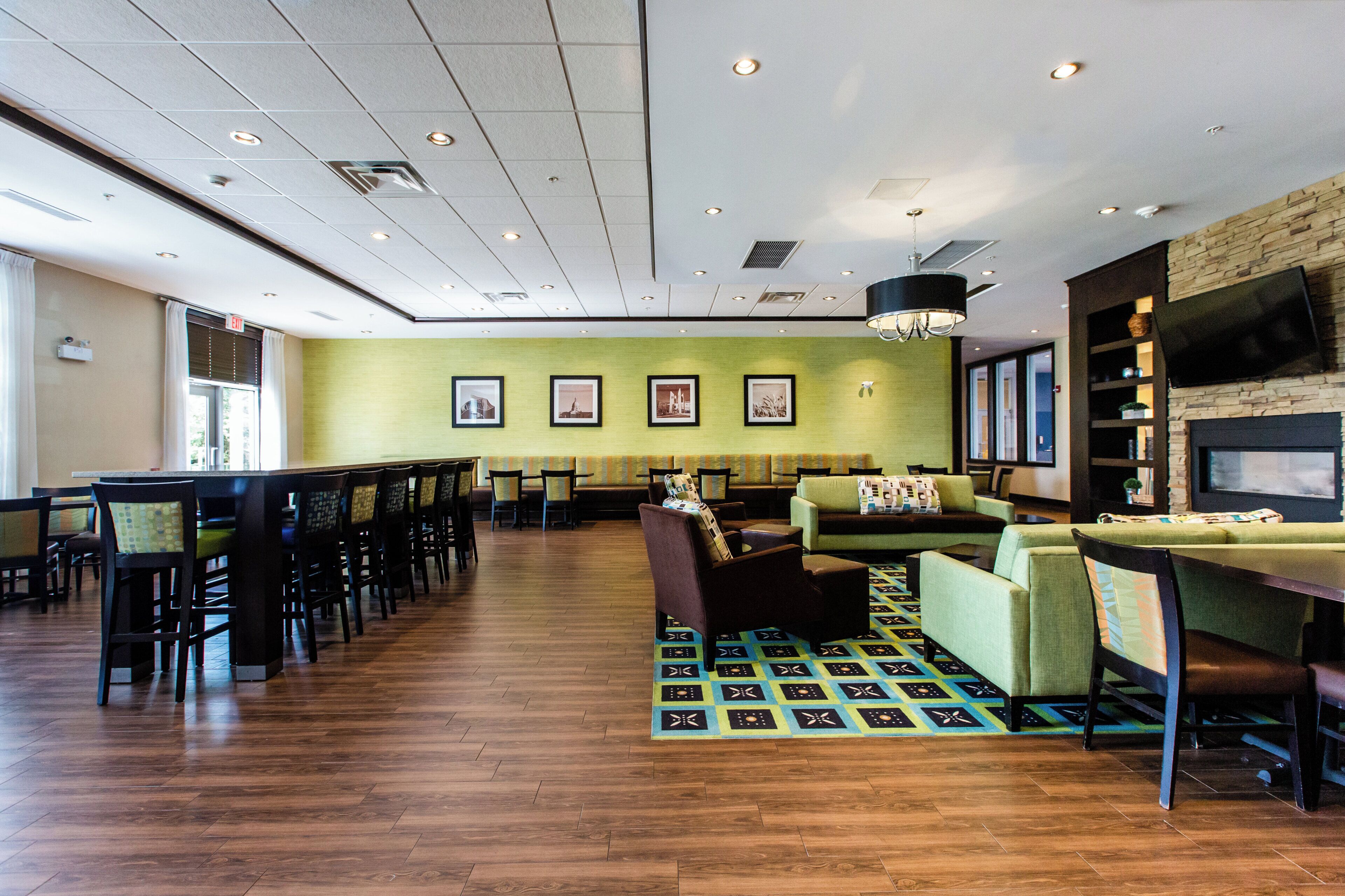 A spacious indoor area with multiple seating arrangements, including tables and chairs, a patterned rug, and a wall-mounted television.