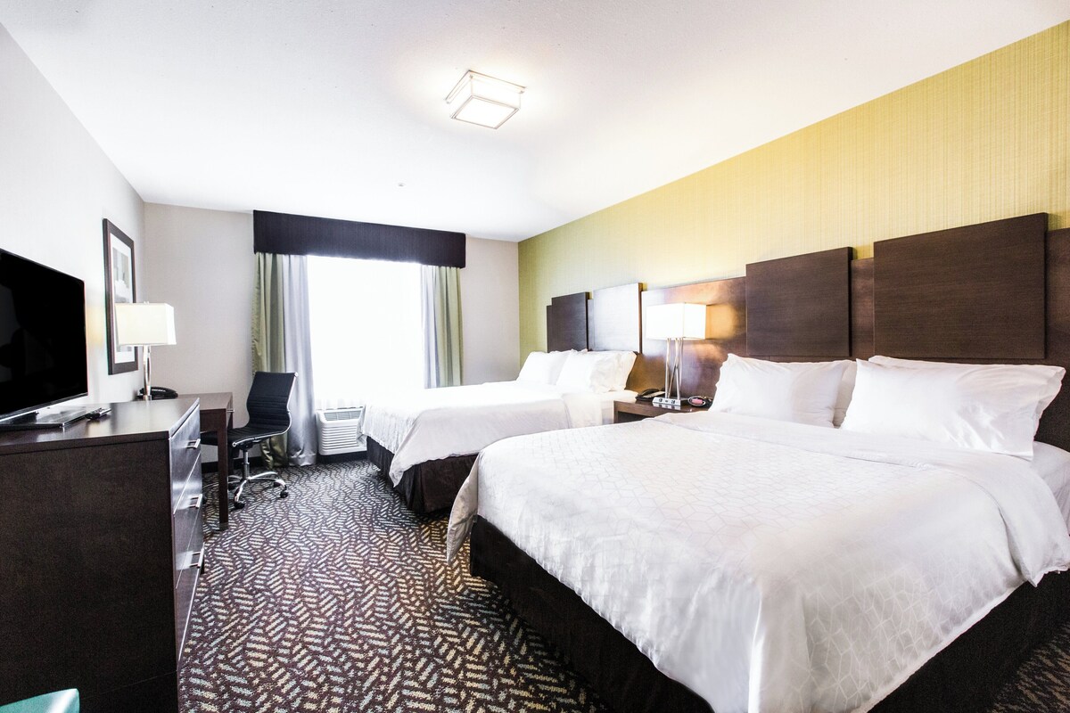 A hotel room with two beds, a desk, a chair, a TV, and a window with curtains.