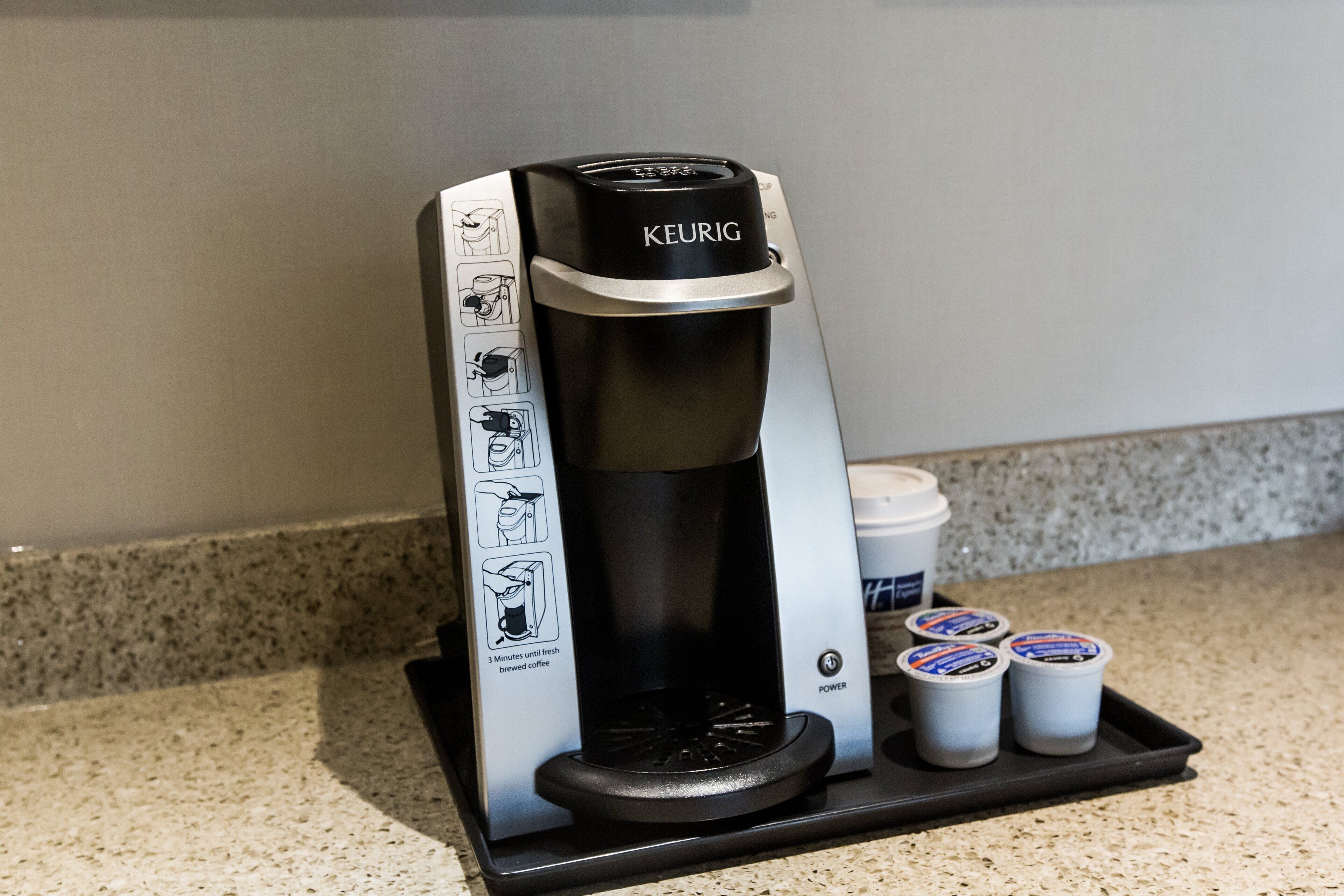 A Keurig coffee maker with instructions, a power button, and three coffee pods on a countertop.