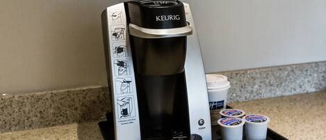 A Keurig coffee maker with instructions, a power button, and three coffee pods on a countertop.