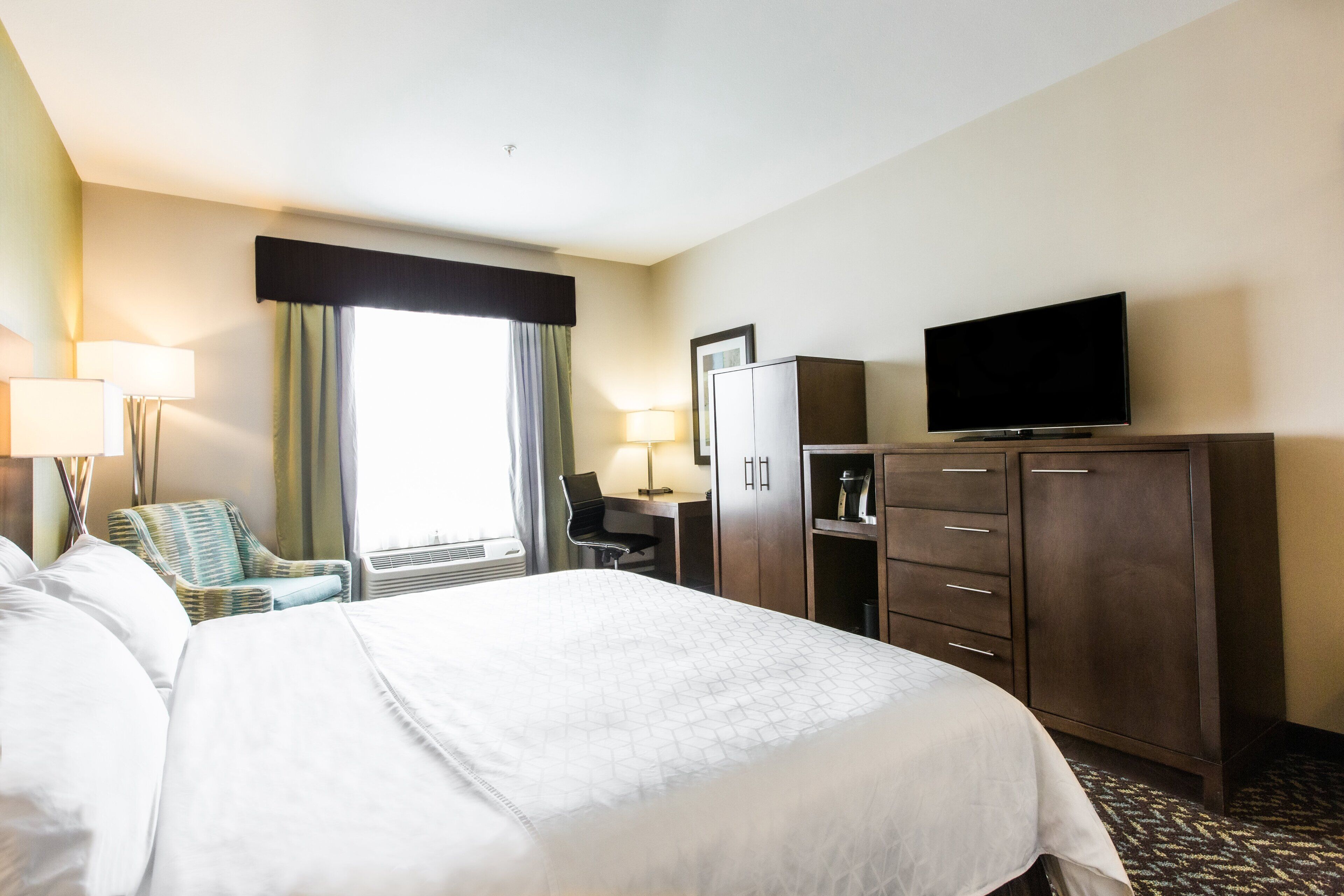 A hotel room with a large bed, a desk with a chair, a television, and a wardrobe.