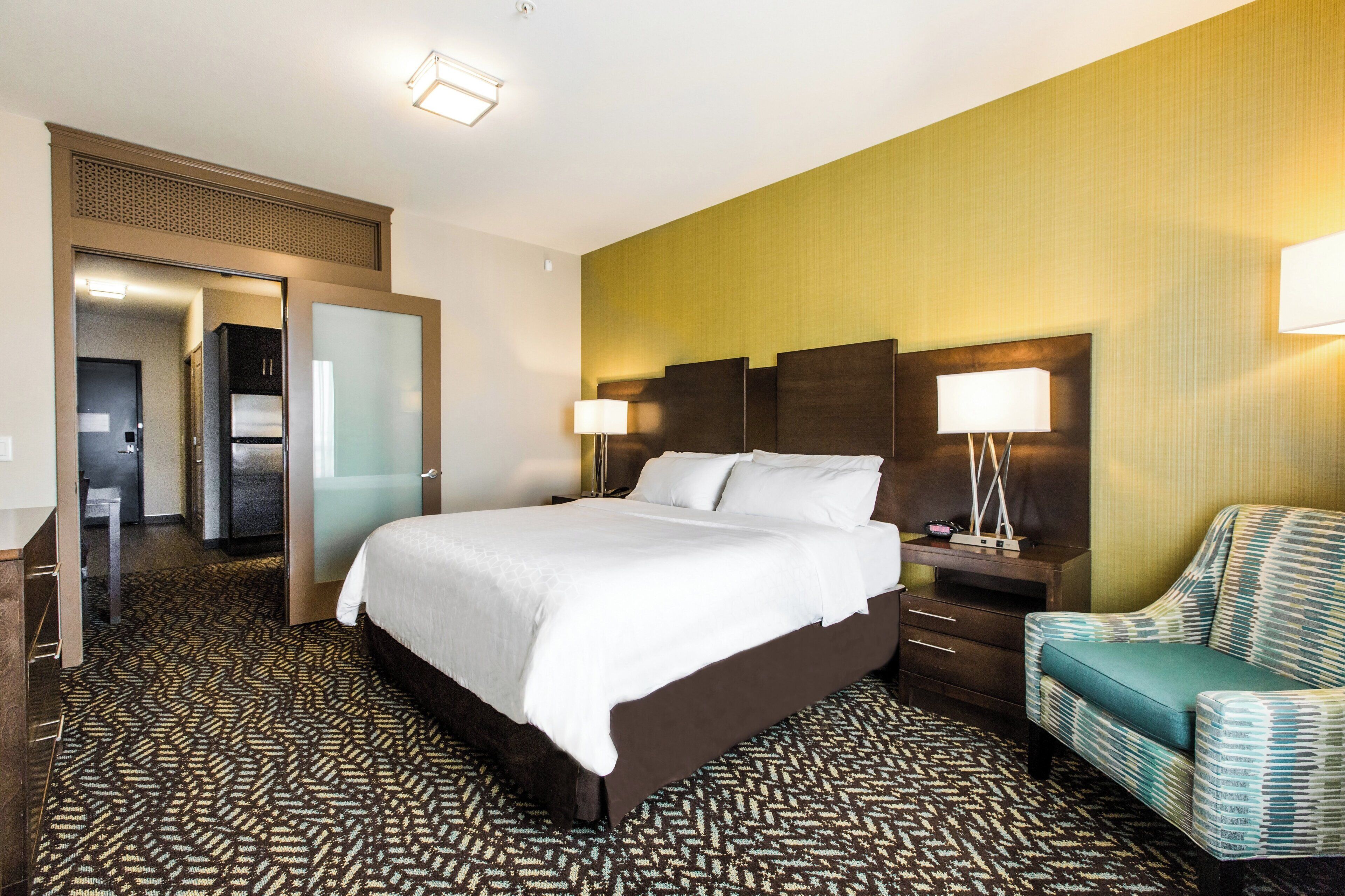 A hotel room with a large bed, a nightstand, a chair, and a door leading to a bathroom.