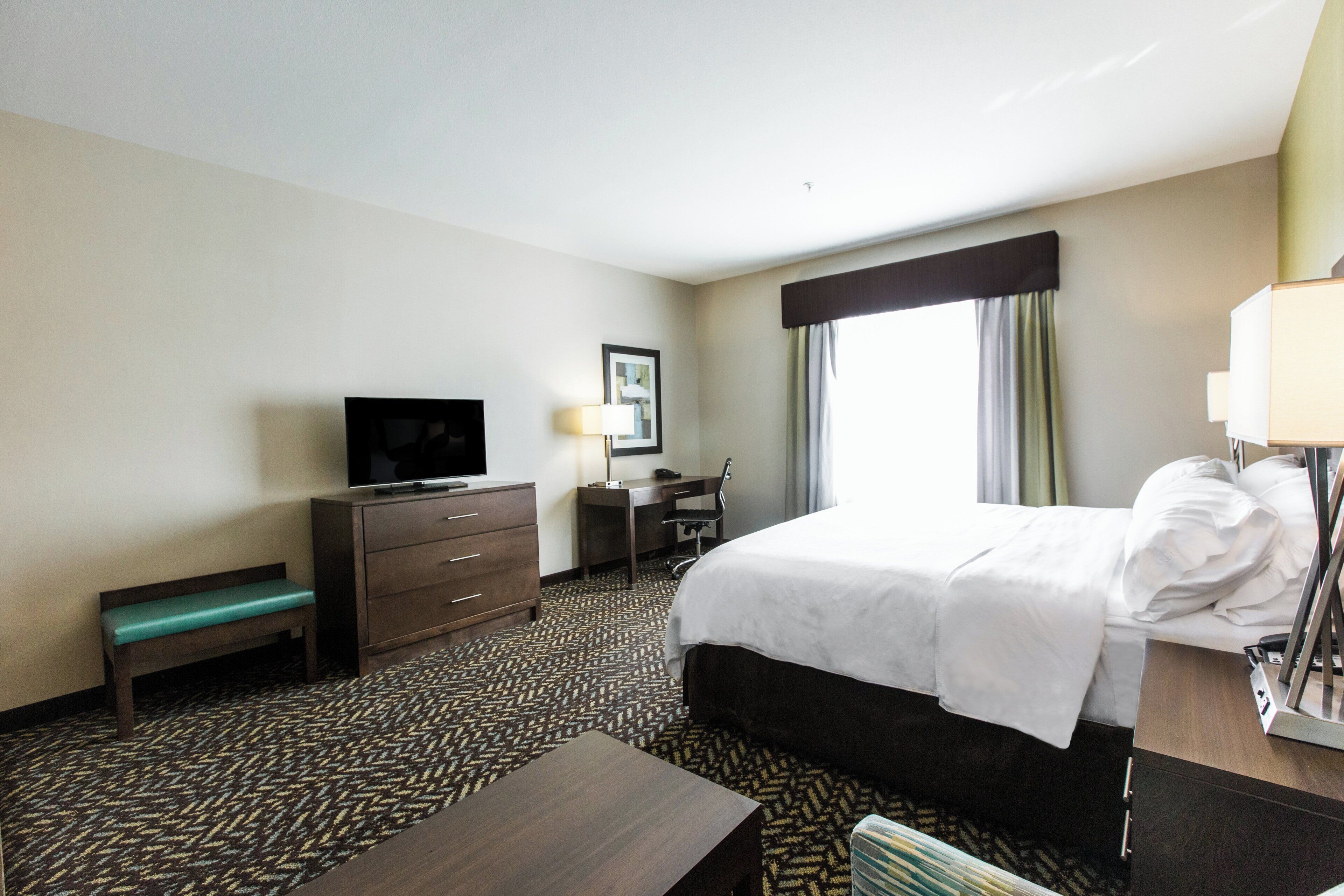 A hotel room with a bed, a desk, a television, and a window with curtains.