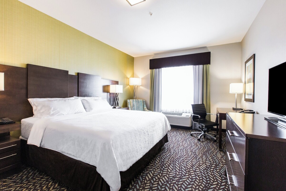 A hotel room with a large bed, a desk, a chair, and a TV.