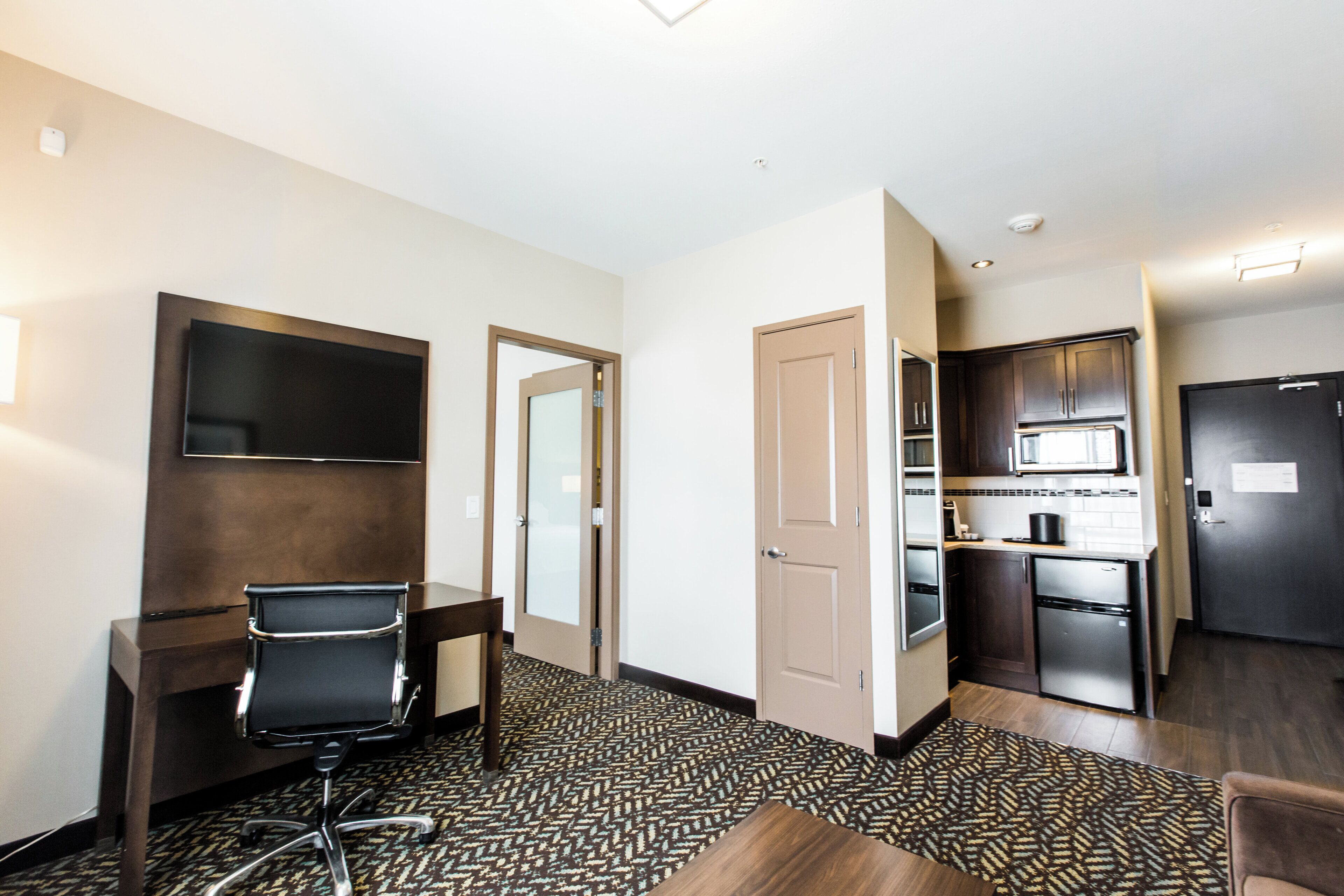 Een hotelkamer met een bureau, stoel, kitchenette en een aan de muur bevestigde televisie.