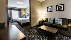 A hotel room with a bed, a sofa, a coffee table, and two lamps. There is a window with curtains and a door leading to another room. - Holiday Inn Express & Suites Spruce Grove - Stony Plain by IHG (Spruce Grove)