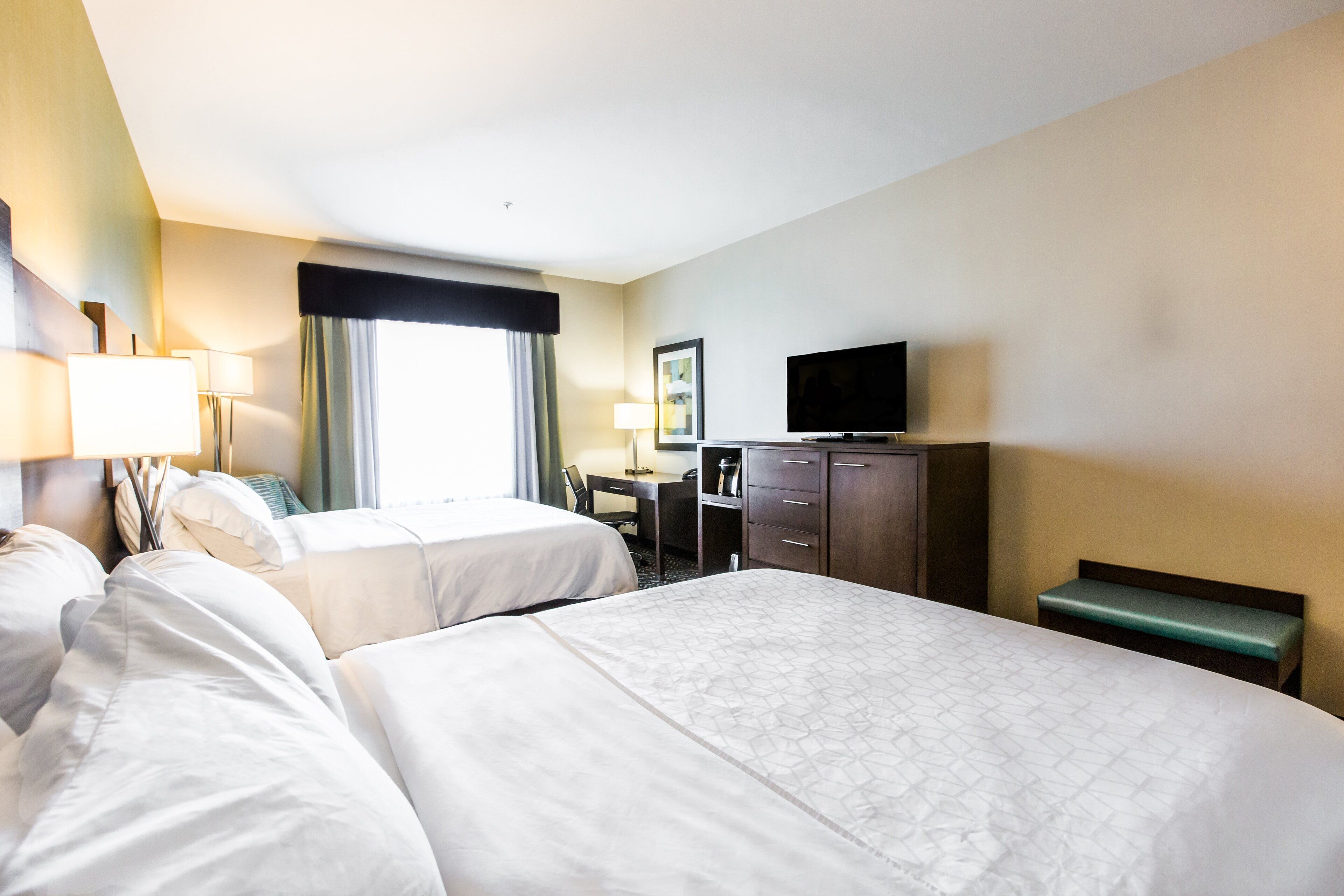 A hotel room with two beds, a desk, a television, and a window with curtains.