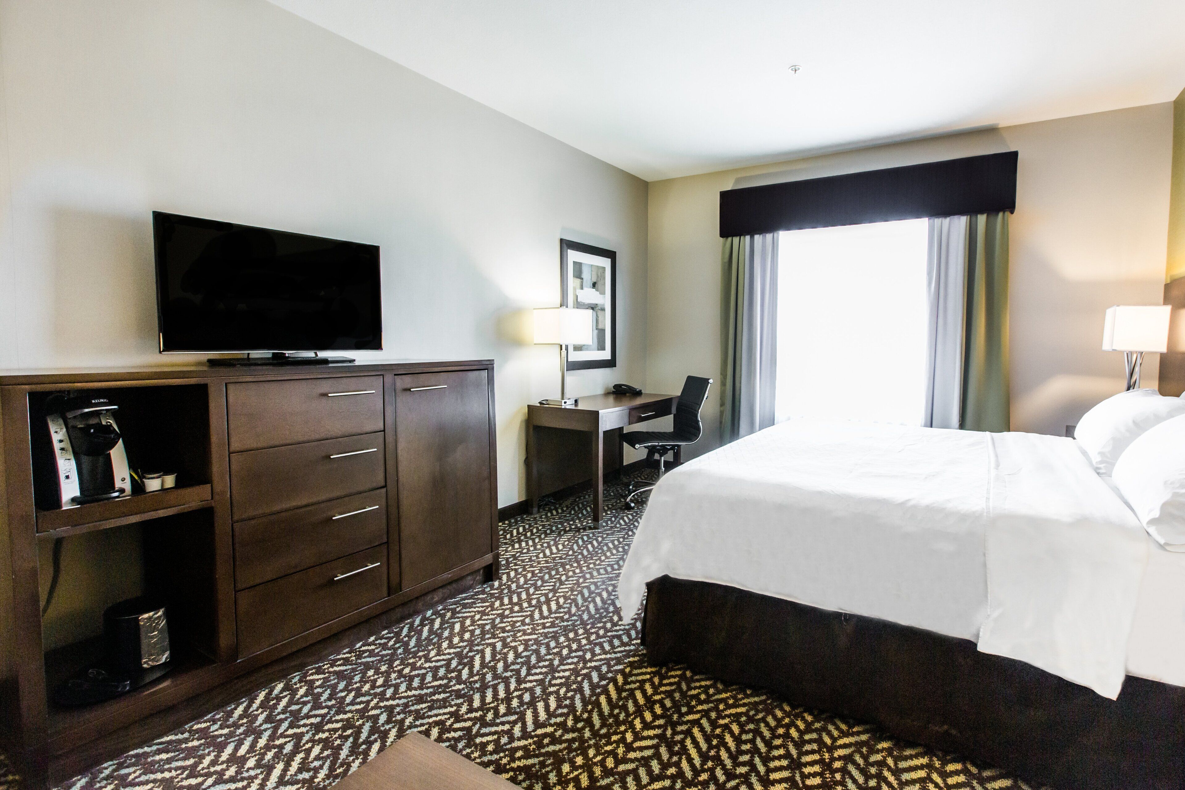A hotel room with a bed, a desk, a television, and a coffee machine.