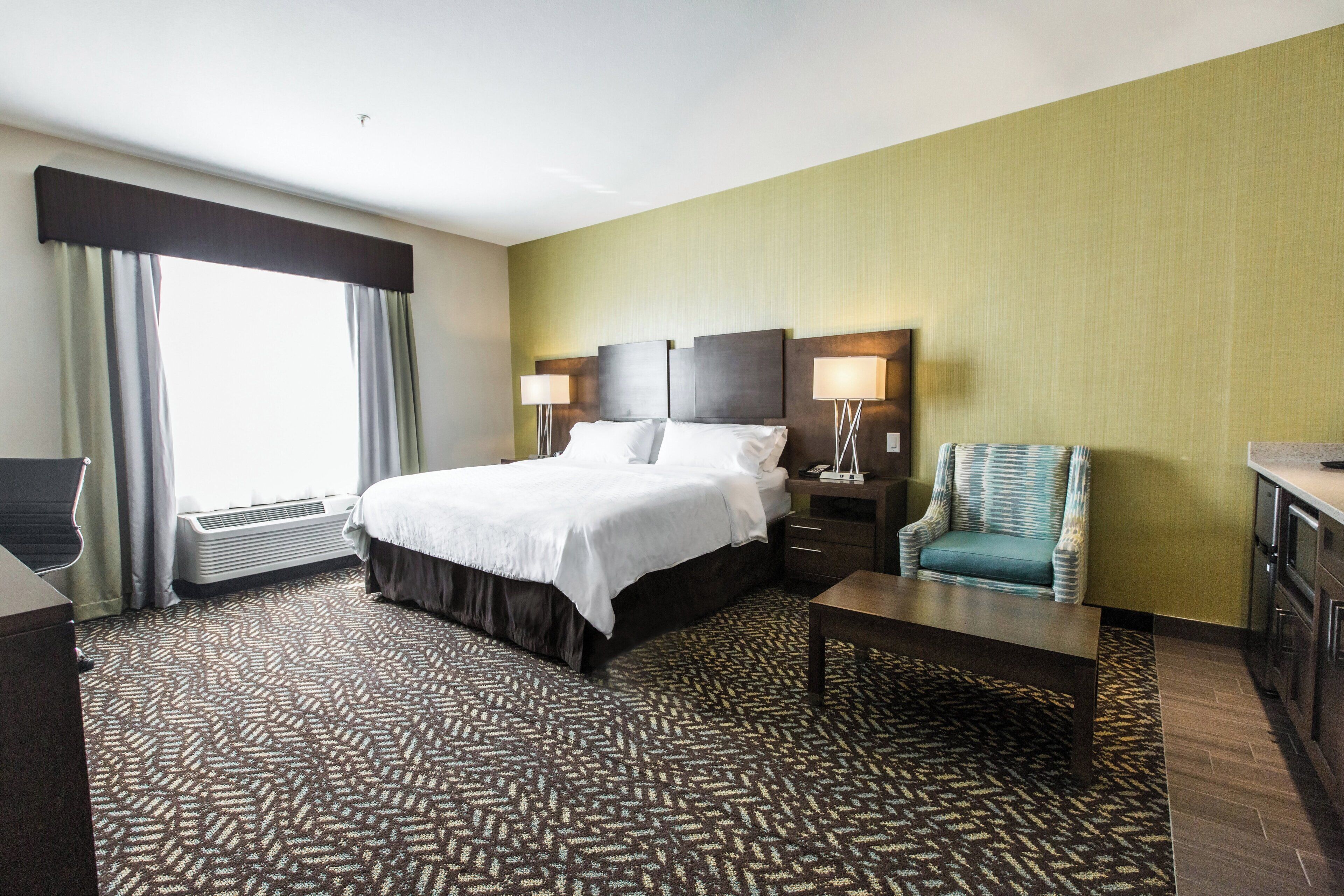 A hotel room with a large bed, two bedside lamps, a chair, a desk, and a window with curtains.