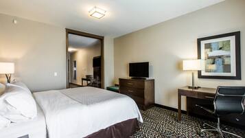A hotel room with a bed, a desk with a chair, a television, and a framed picture on the wall.