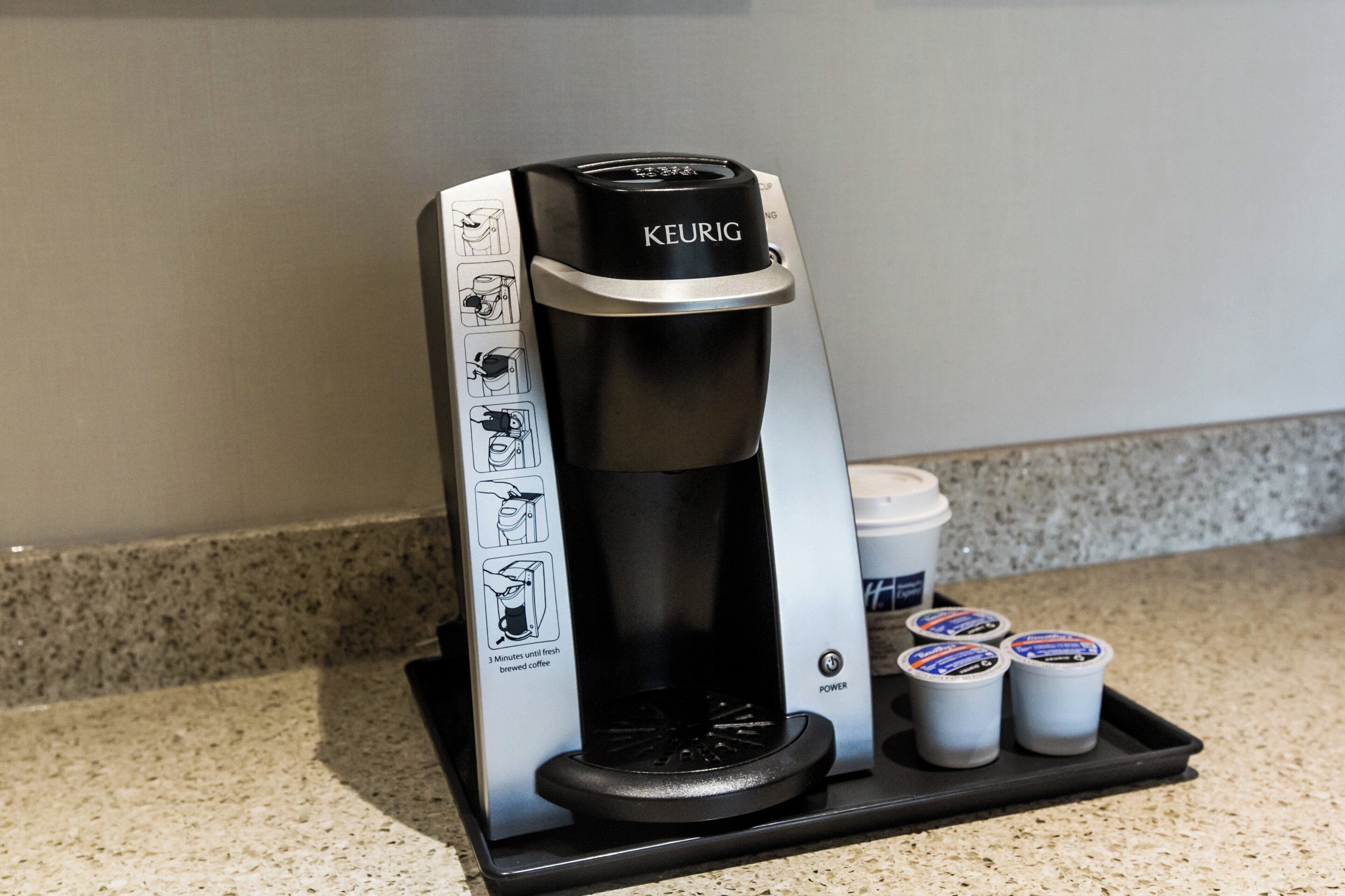 A Keurig coffee maker with instructions, a power button, and three pods on a countertop.