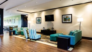 A modern hotel lobby with a wooden floor, teal sofas, striped armchairs, and a flat-screen TV on the wall. - Holiday Inn Express & Suites Spruce Grove - Stony Plain by IHG (Spruce Grove)