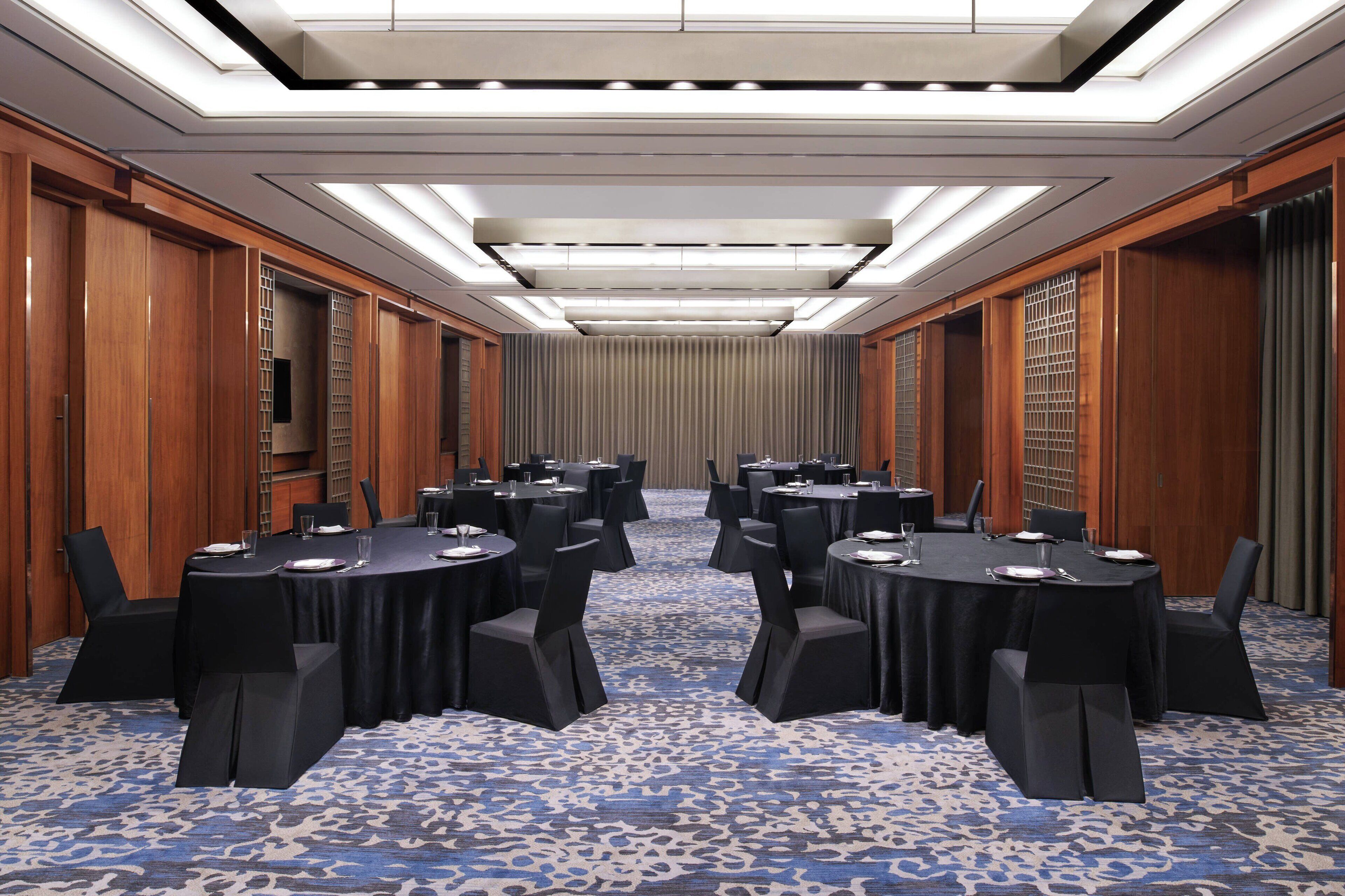 Un salón de conferencias con varias mesas redondas, sillas negras y una alfombra estampada.