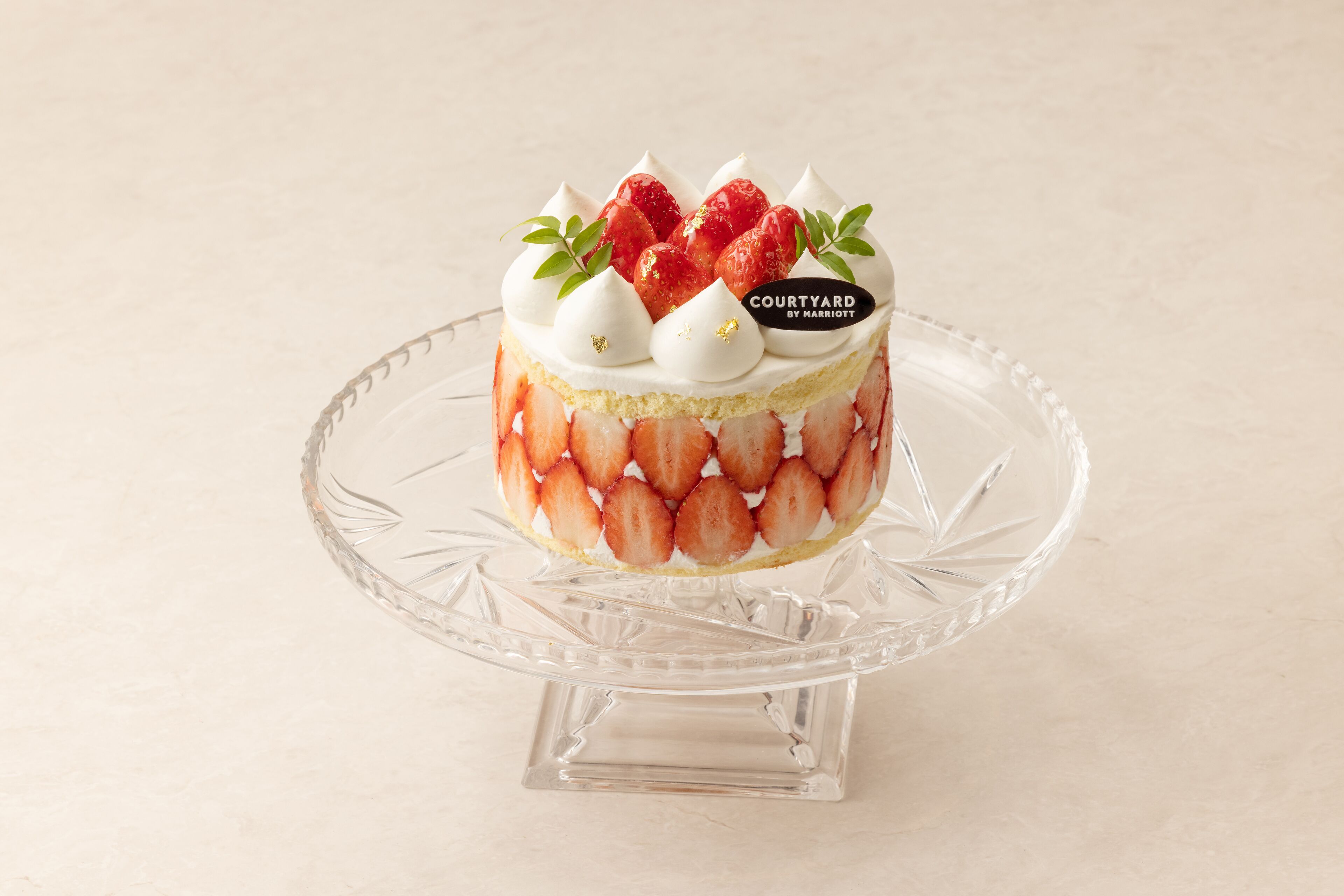 A cake on a clear glass stand with strawberries and white cream on top.