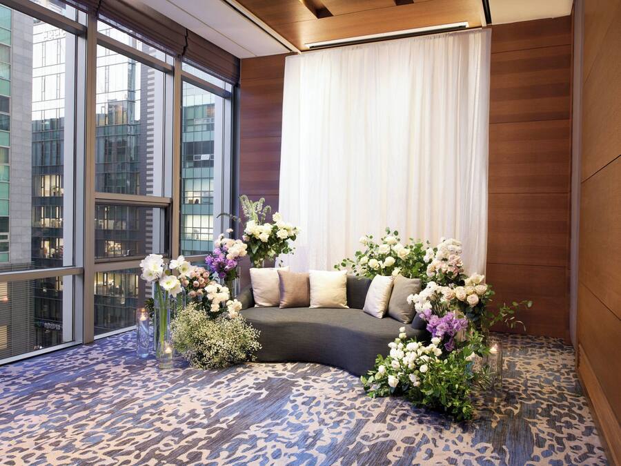 A modern hotel room with a curved sofa, large windows, and a patterned carpet.