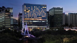 A modern hotel with a prominent glass facade, a central atrium, and a decorative bridge structure.