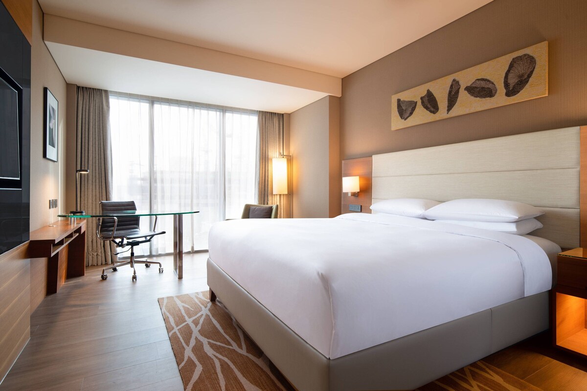 Una habitación de hotel con una cama grande, un escritorio con una silla, un televisor y una ventana con cortinas.