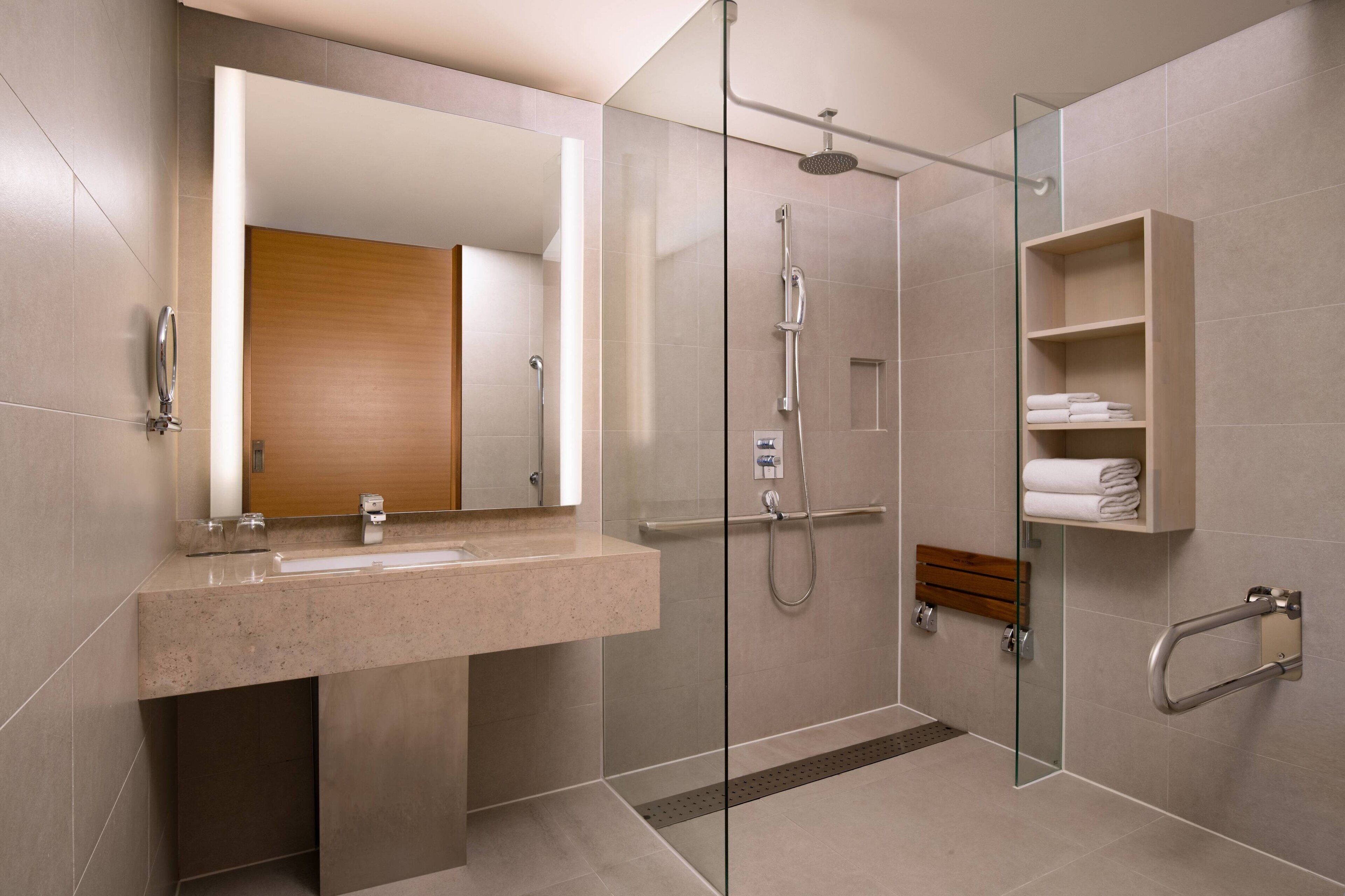 Un baño moderno con ducha de vidrio, lavamanos con espejo y un perchero para toallas.