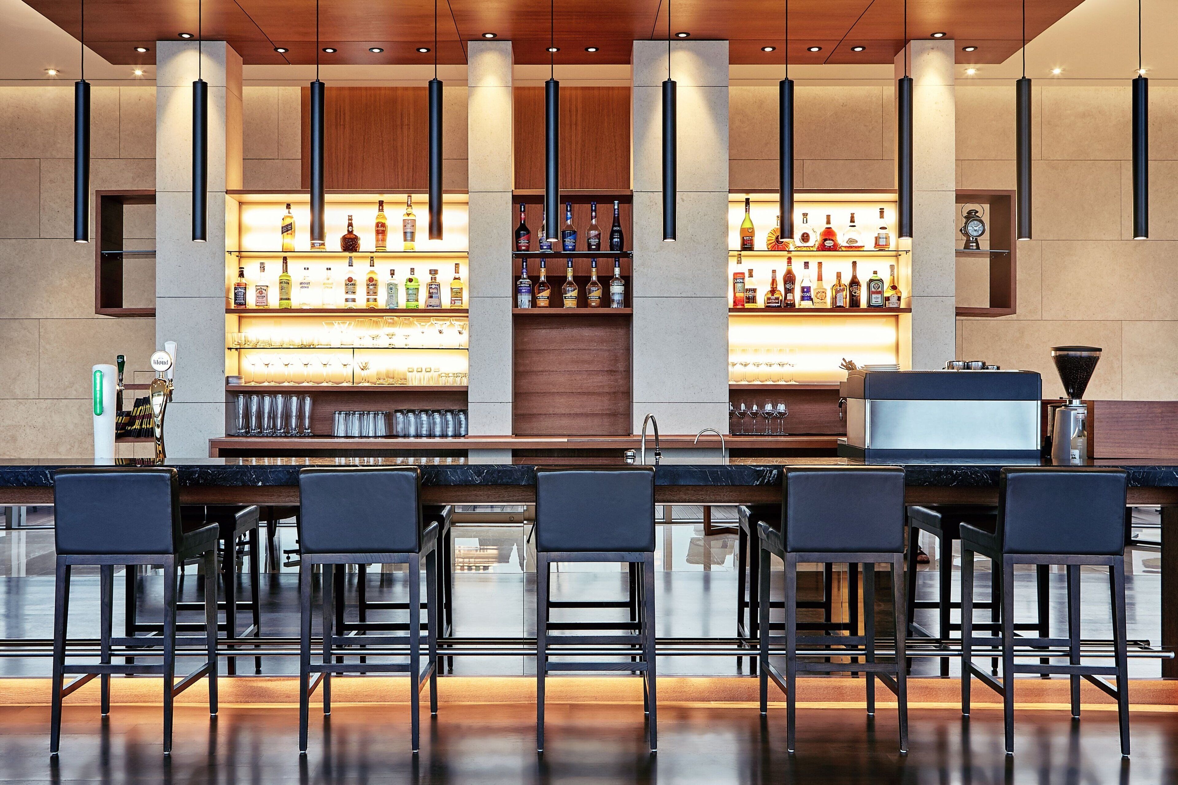 A bar area with multiple stools, a well-lit shelf with bottles, and a modern design.