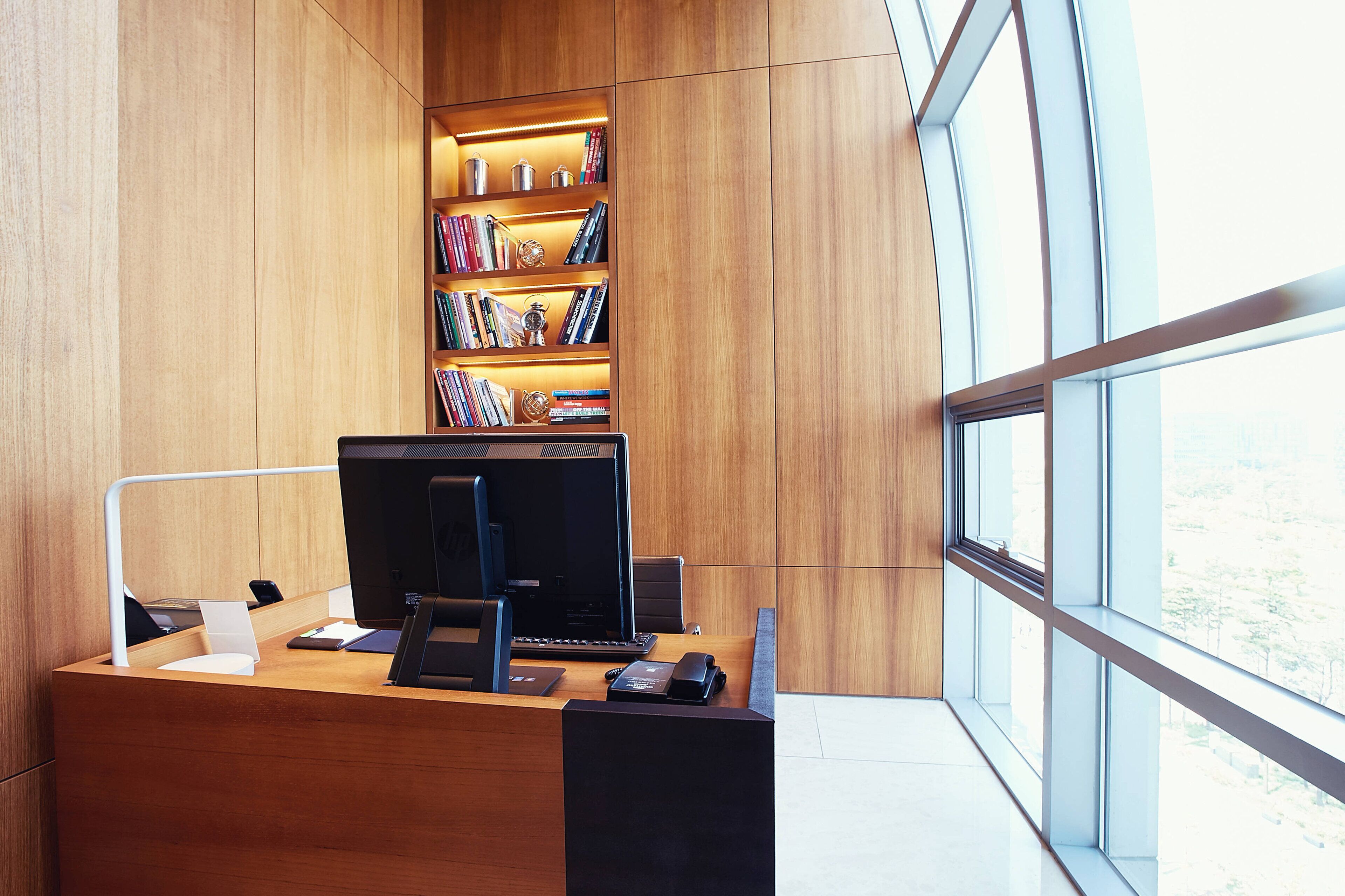 Ein modernes Büro mit einem Holztisch, Computer und Regalen mit Büchern und Pokalen.
