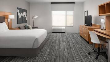 A hotel room with a bed, desk, chair, TV, and artwork.