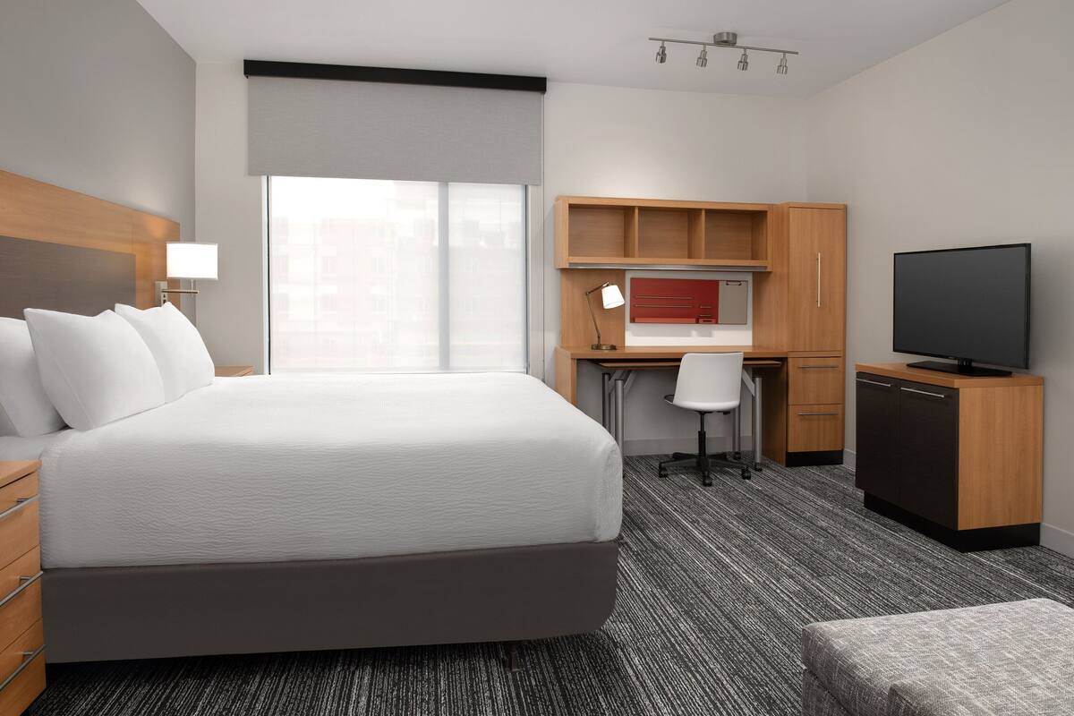 A hotel room with a large bed, a desk, a television, and a wardrobe.