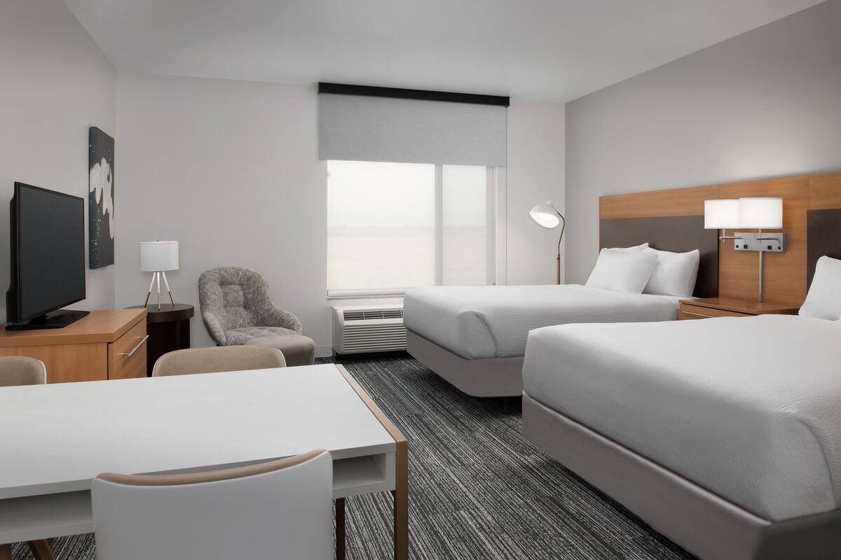 A hotel room with two beds, a desk, a chair, a television, and a window with a view.