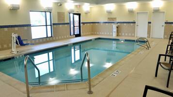 An indoor swimming pool with clear lane markings, safety railings, and adjacent seating areas.