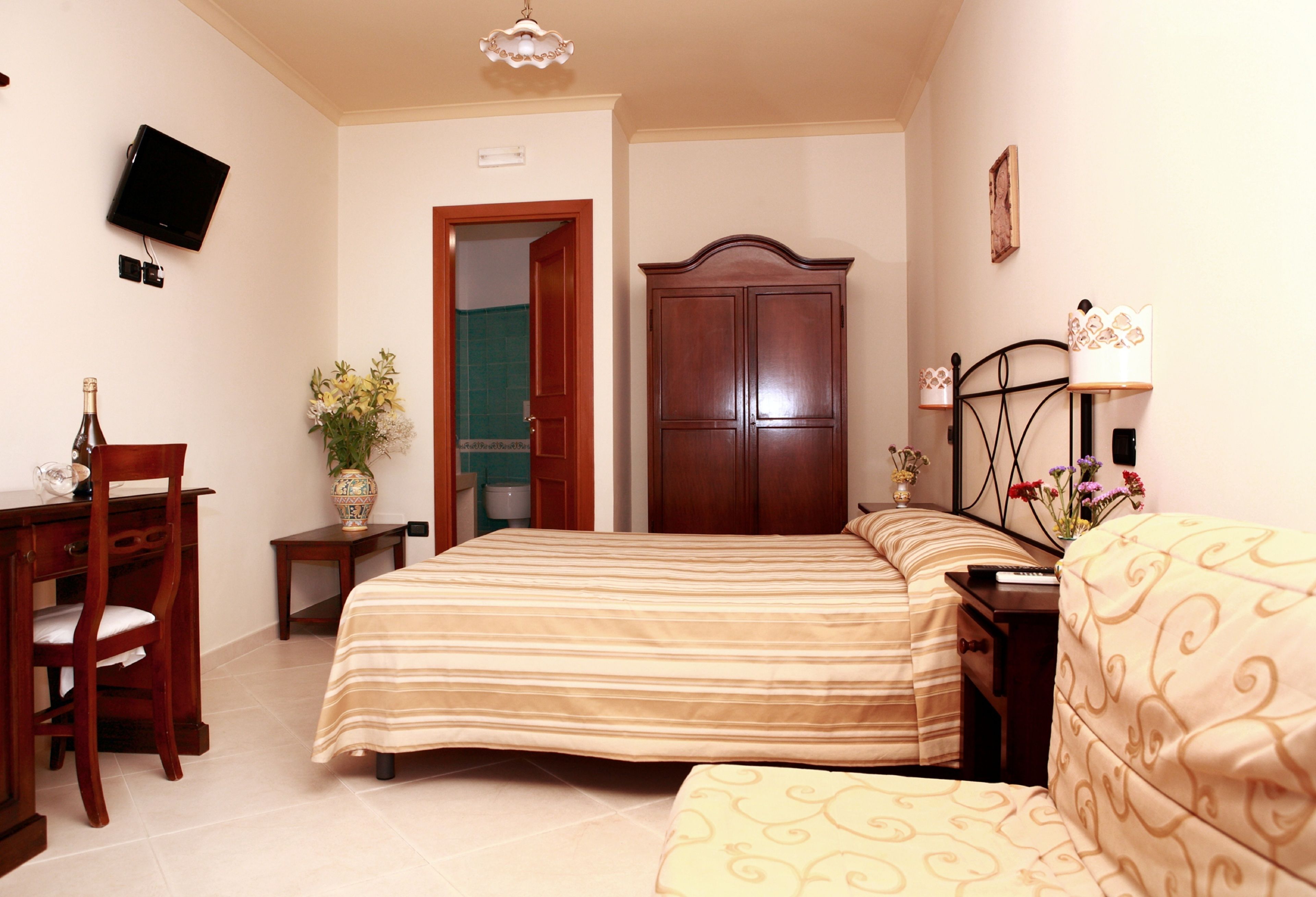 A bedroom with a bed, a desk, a chair, a wardrobe, and a television.