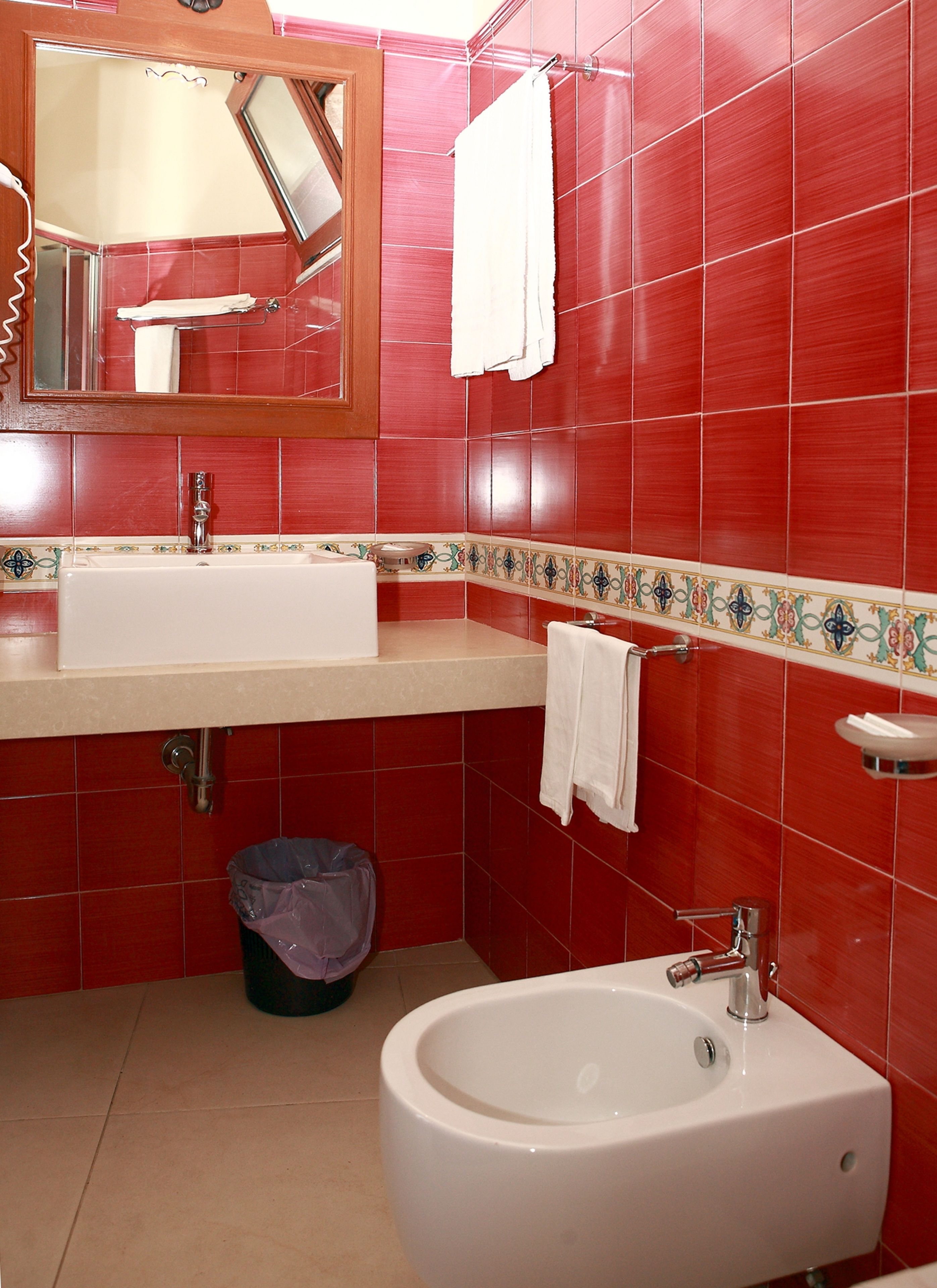 A bathroom with red tiles, a white sink, a mirror, and a bidet.