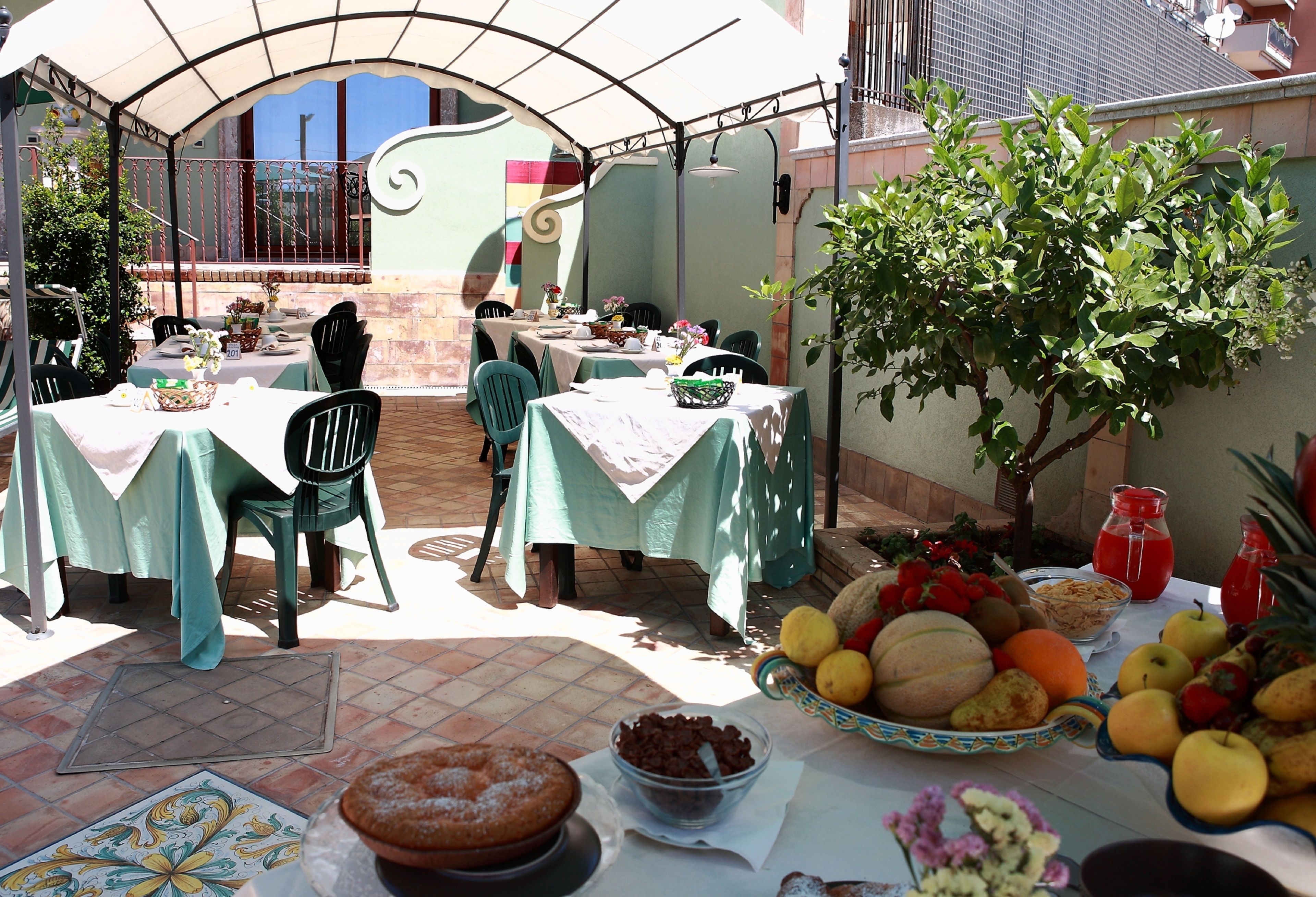 An outdoor patio with tables set for dining, surrounded by a garden and a decorative wall.