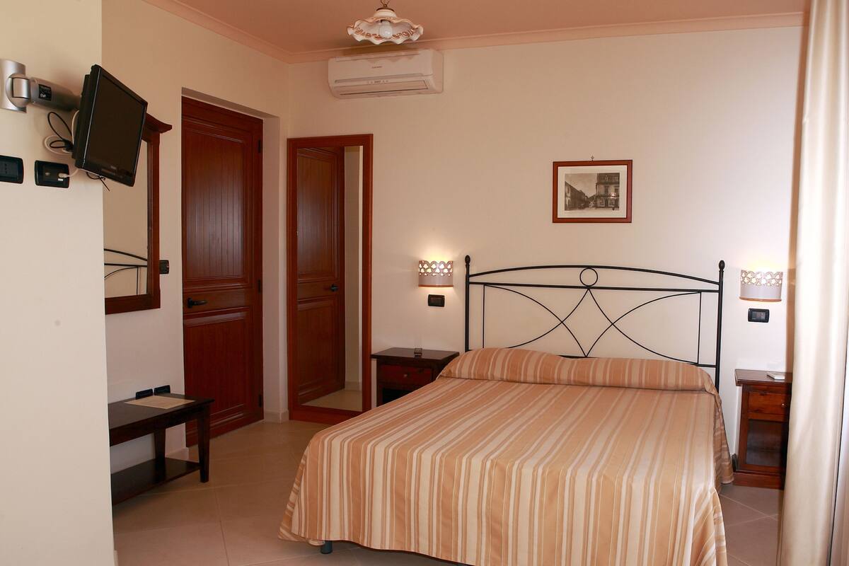 A bedroom with a bed, a desk, a chair, a television, and a door.