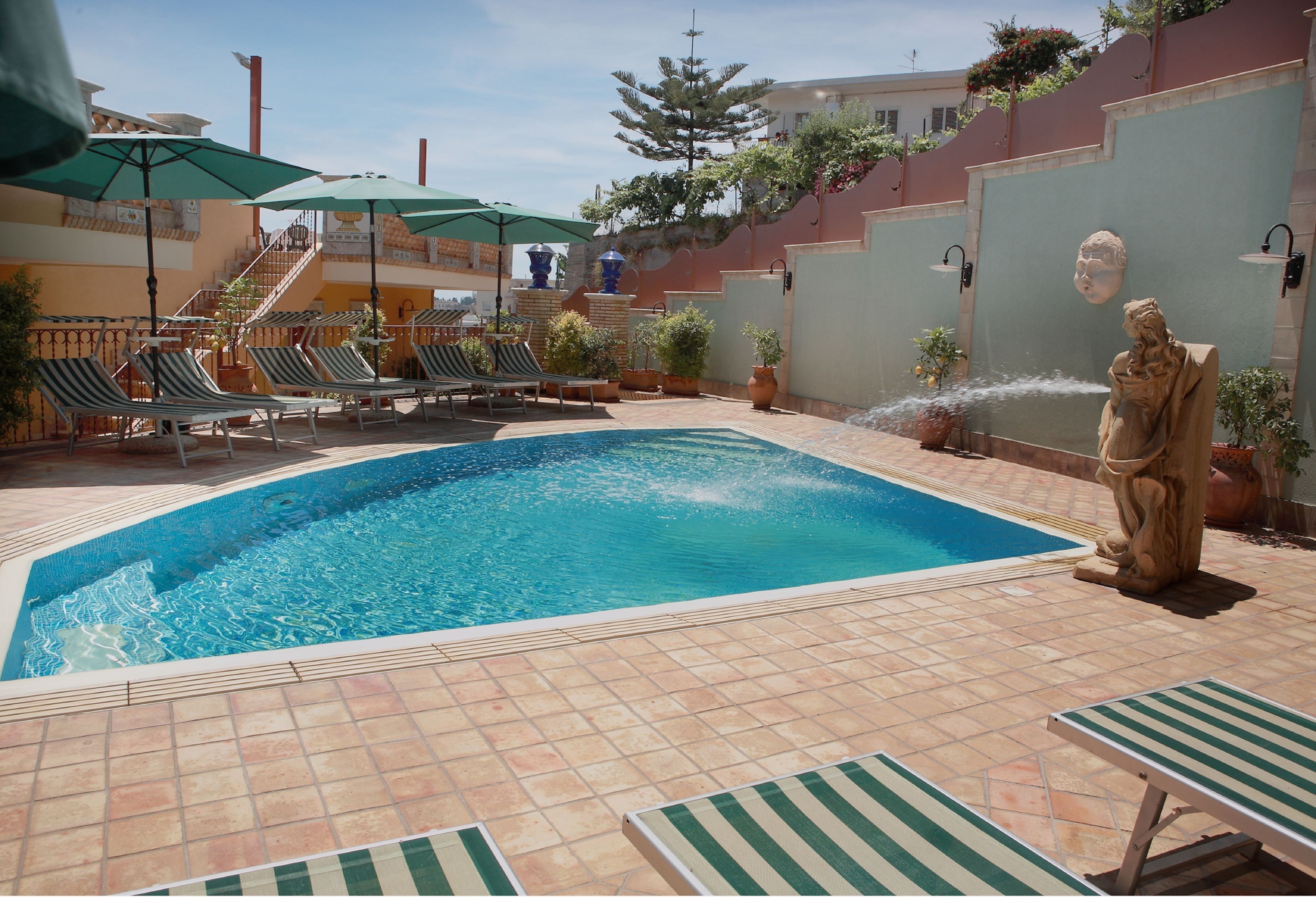 A swimming pool with lounge chairs and umbrellas, surrounded by potted plants and a statue.