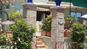 Een binnenplaats met een grote terracotta pot, een trap die naar een balkon leidt, en een bord met daarop een bar.