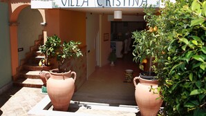 Een villa genaamd 'Villa Cristina' met een betegelde entree, planten in potten en een trap die naar binnen leidt.