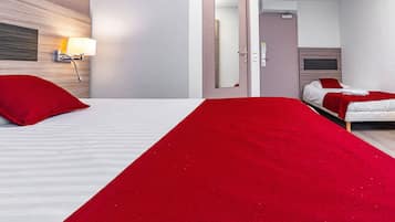 Habitación de hotel con dos camas, una manta roja, una mesita de noche con lámpara y un espejo.