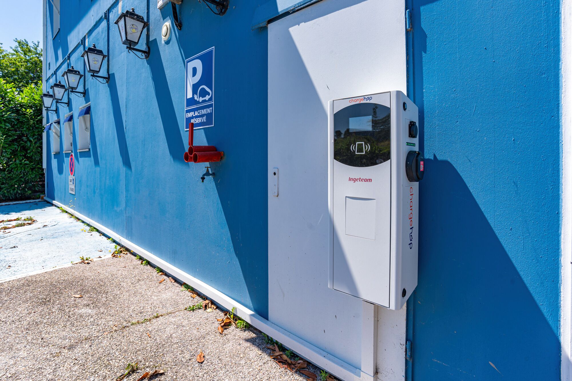 A blue building with a parking sign, a charging station, and a door with a lock.