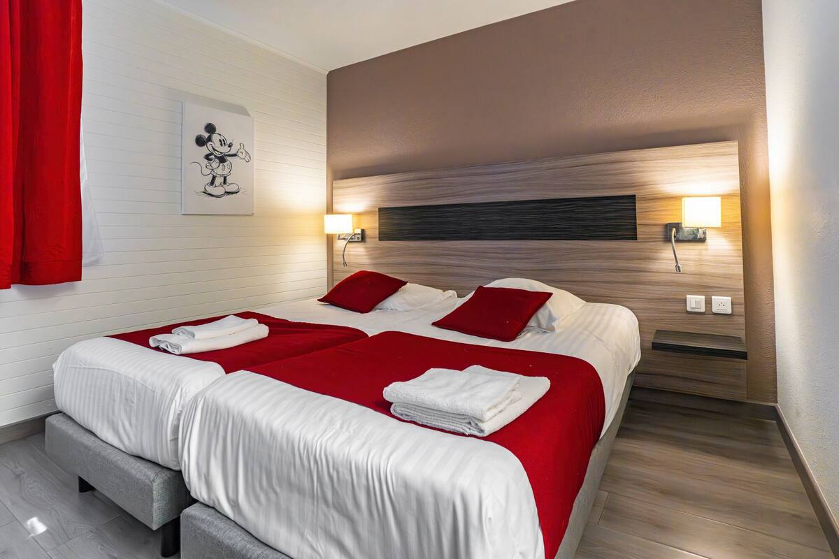 A hotel room with a large bed, two bedside tables, and a red curtain.