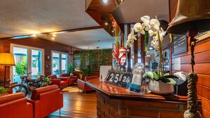 Un vestíbulo de hotel con chimenea de ladrillo, sofás de cuero rojo, suelo de madera y una pared verde con plantas.