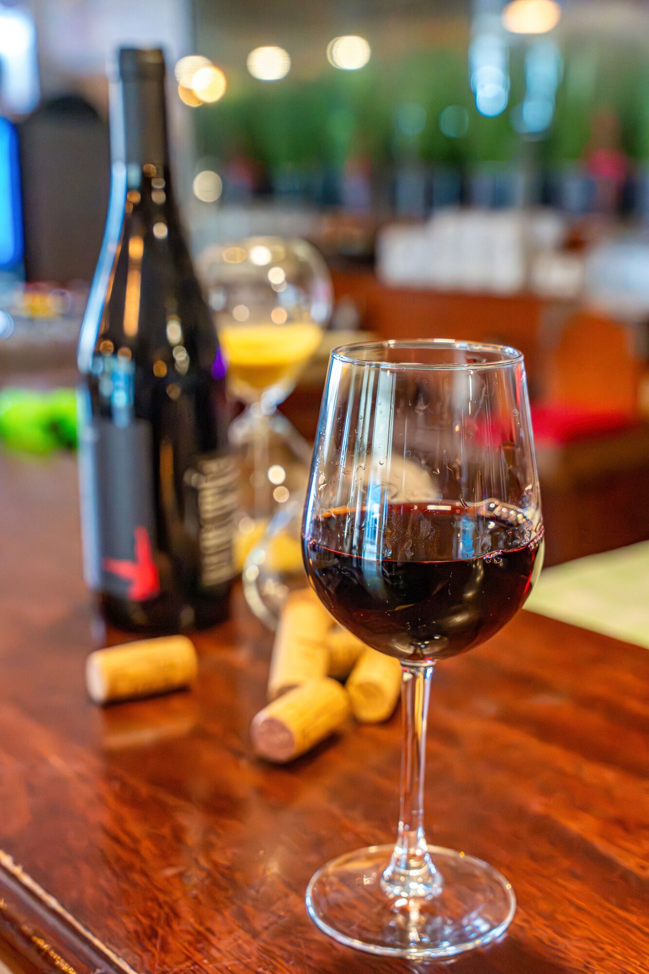 Ein Weinglas mit Rotwein auf einem Holztisch, im Hintergrund eine Weinflasche und Korken.