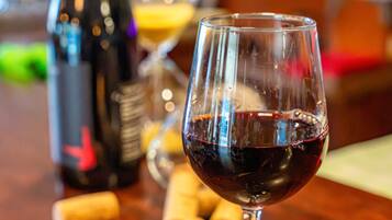 Ein Weinglas mit Rotwein auf einem Holztisch, im Hintergrund eine Weinflasche und Korken.