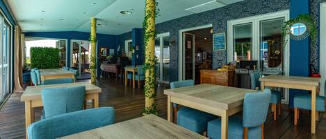 A restaurant with wooden tables and blue chairs, a blue and white patterned wall, and a large mirror.