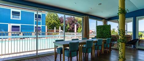 Ein geräumiges Zimmer mit großem Fenster mit Blick auf einen Pool und ein blaues Gebäude.