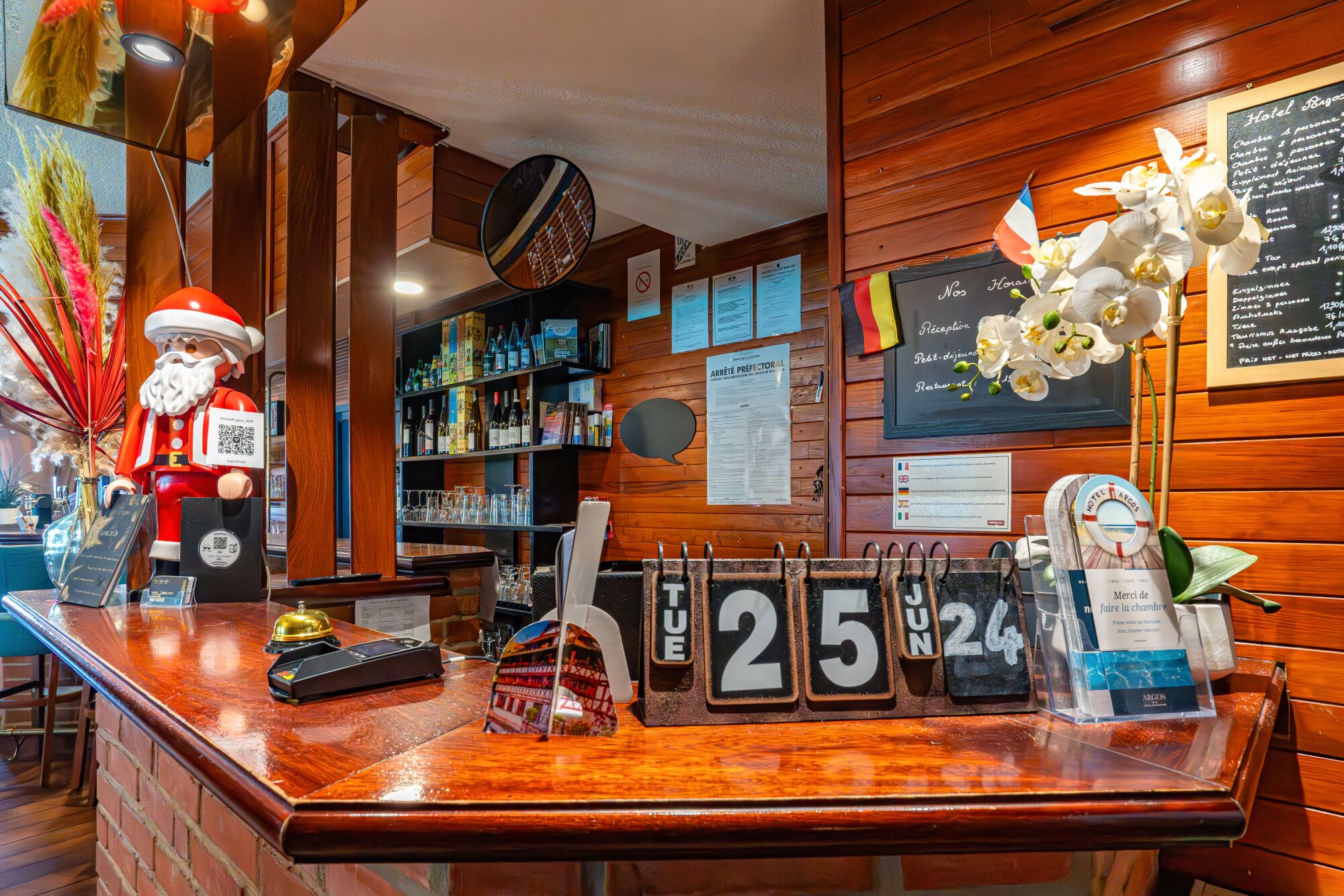 Un espace d’accueil d’hôtel avec un intérieur en bois, une horloge, un calendrier et un code QR sur le comptoir.