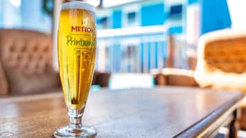 A glass of beer with "METEO" and "Pintemps" on it, placed on a wooden table in a room with a blurred background.
