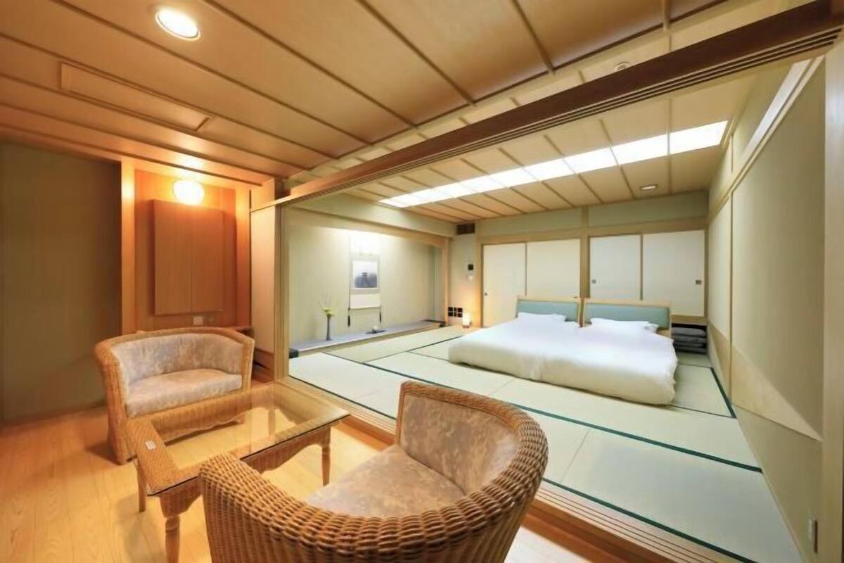 A traditional Japanese-style room with tatami flooring, a low bed, a wooden cabinet, and a wicker chair.