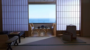 Una habitación japonesa tradicional con suelo de tatami, una mesa baja con un set de té y vistas al océano a través de puertas shoji.