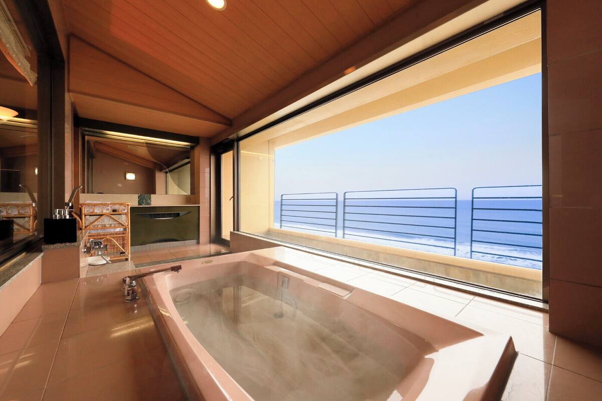 A modern bathroom with a large bathtub, a glass shower enclosure, and a view of the sea through a large window.