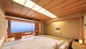 Una habitación con cama, una mesita, una silla, vistas al mar y un estante en la pared con un jarrón.